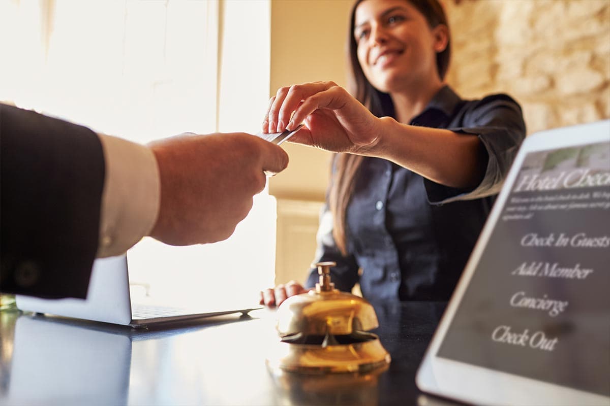 A man's hand as he gives a credit card to a woman working behind the counter at a hotel.