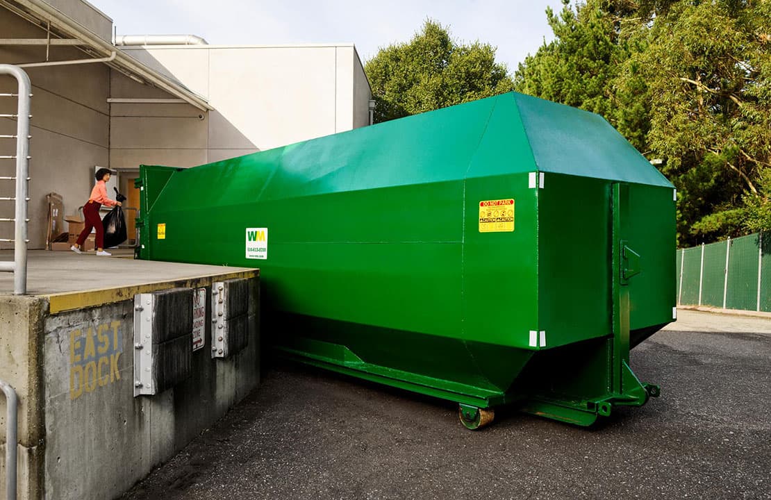 WM customer on loading dock putting materials into a large commercial waste compactor