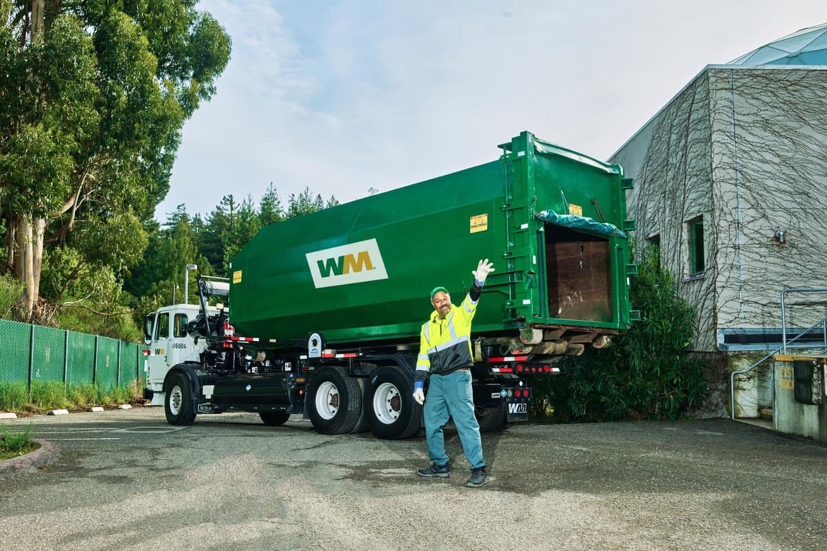 A WM driver waves to customers while removing their commercial compactor.