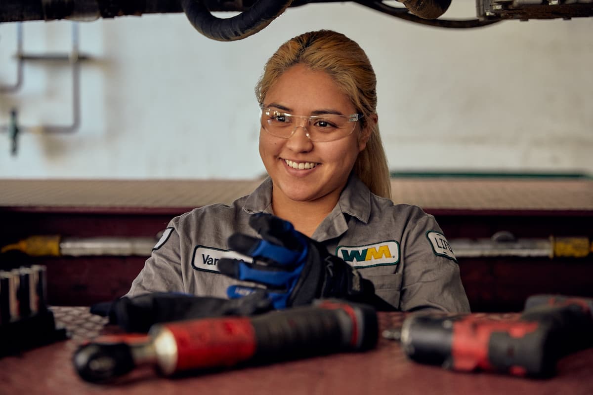 A WM mechanic smiles as she repairs waste management machinery.