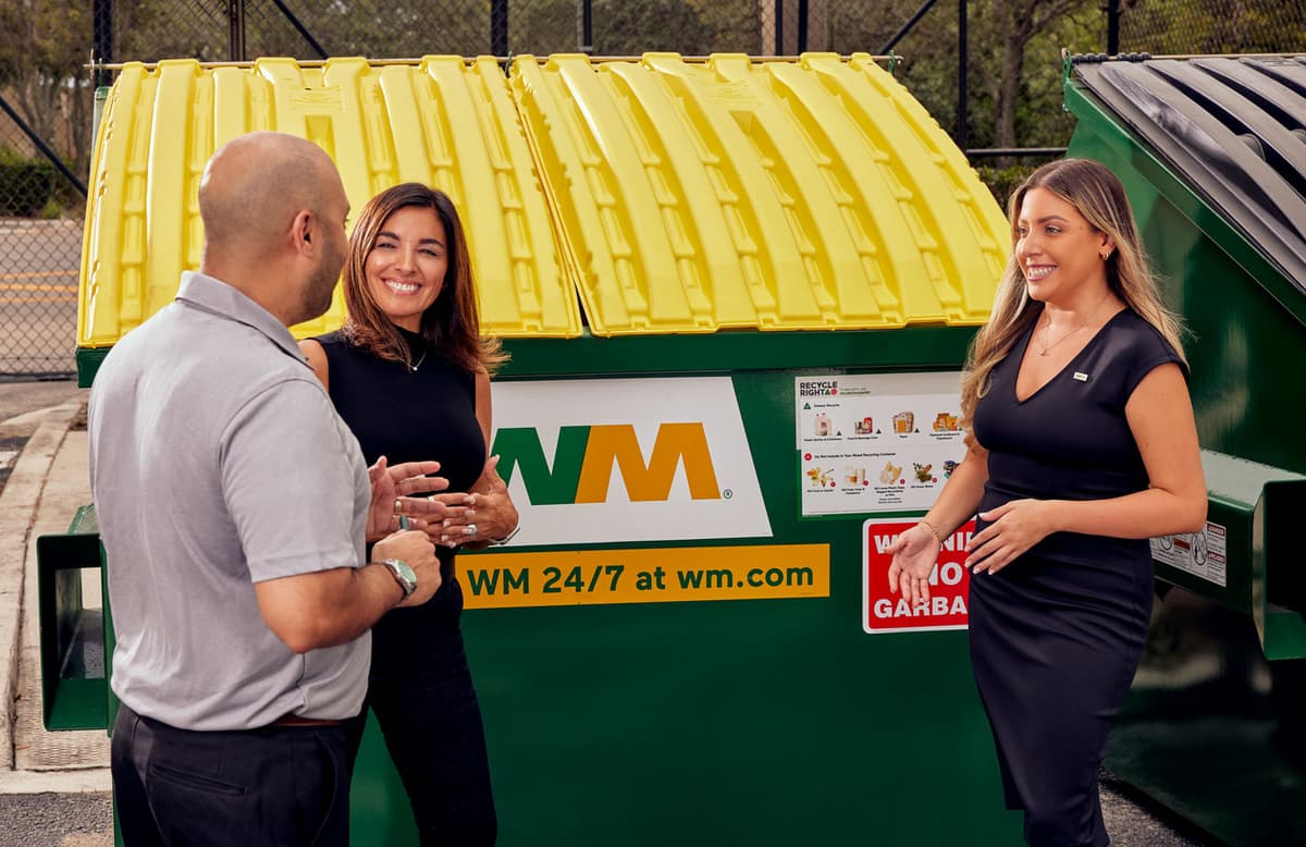 WM Sustainability Advisory team members talk to a client in front of a commercial recycling dumpster