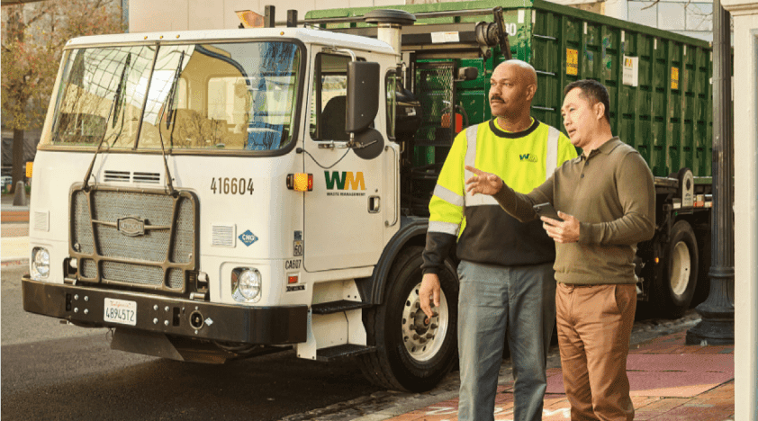 Man having a conversation with a WM employee while standing next to a garbage truck.