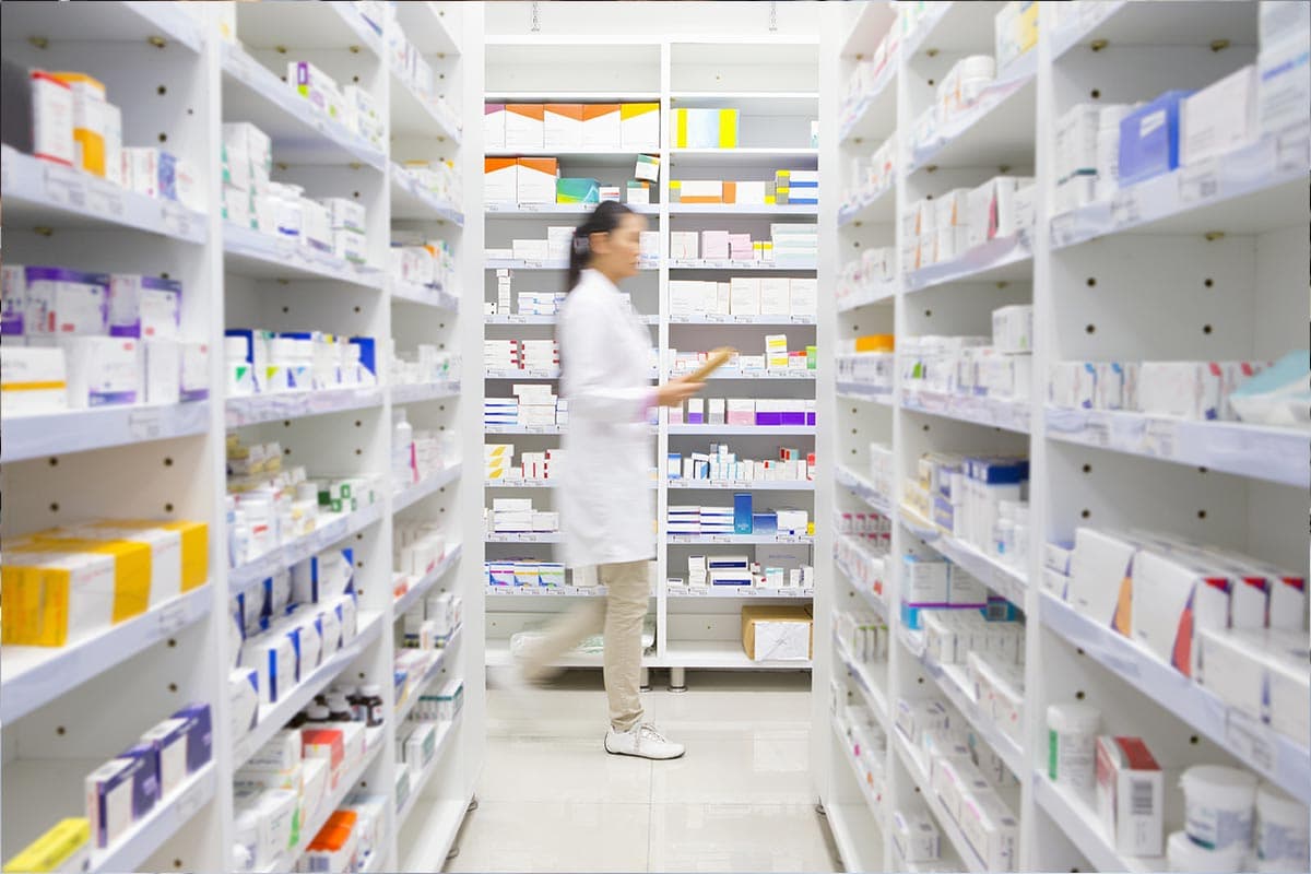 A pharmacist walks through a room with shelves full of prescription medication.