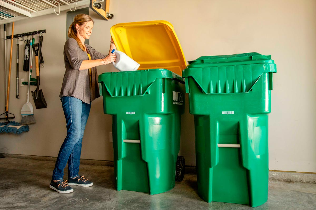 A woman places a plastic container in a Waste Management recycling bin. 